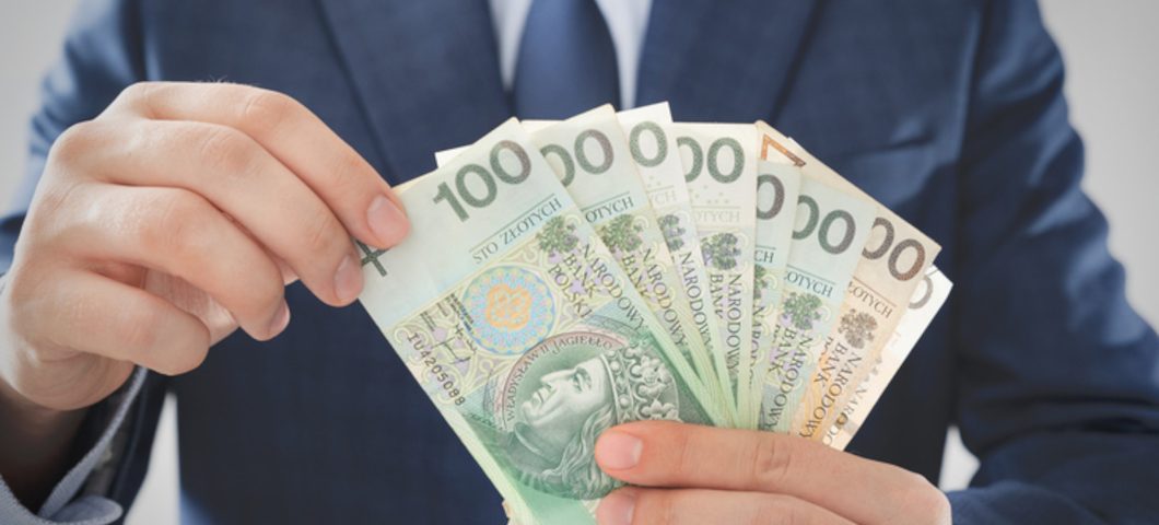 mężczyzna w garniturze trzyma polskie banknoty